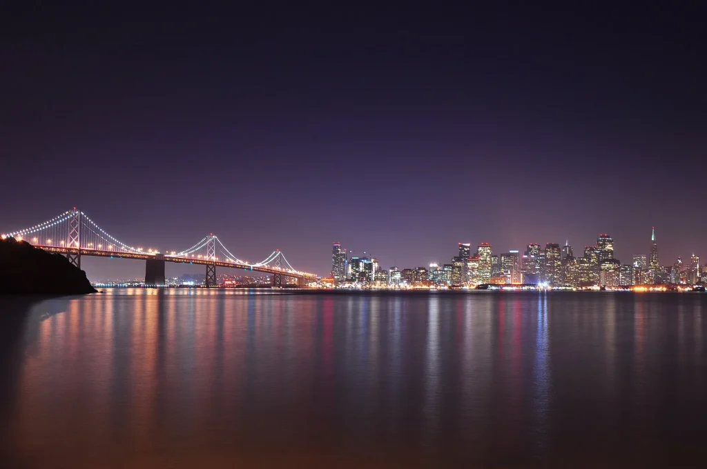 Skyline de San Francisco y el Bay Bridge iluminados de noche, zona de la Bahía donde tramitamos placa temporal en California