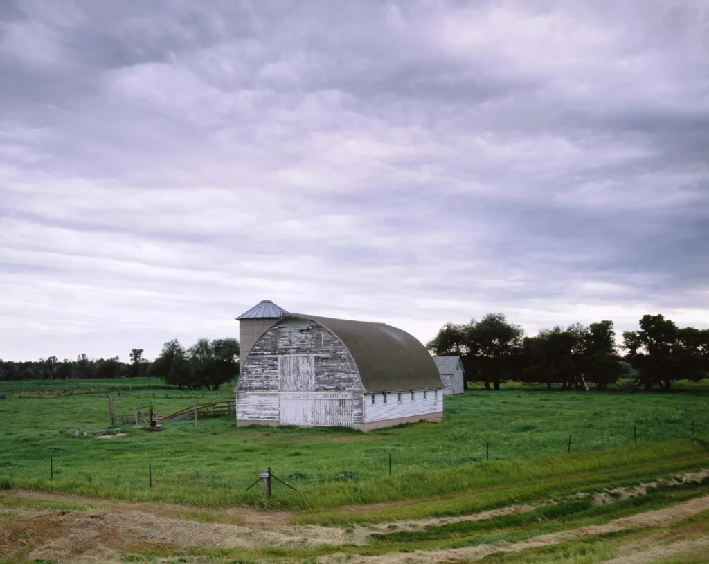 Granero blanco bajo un cielo de tormenta en la pradera rural de Minnesota, zona agrícola donde pedimos la placa temporal en Minnesota por correo