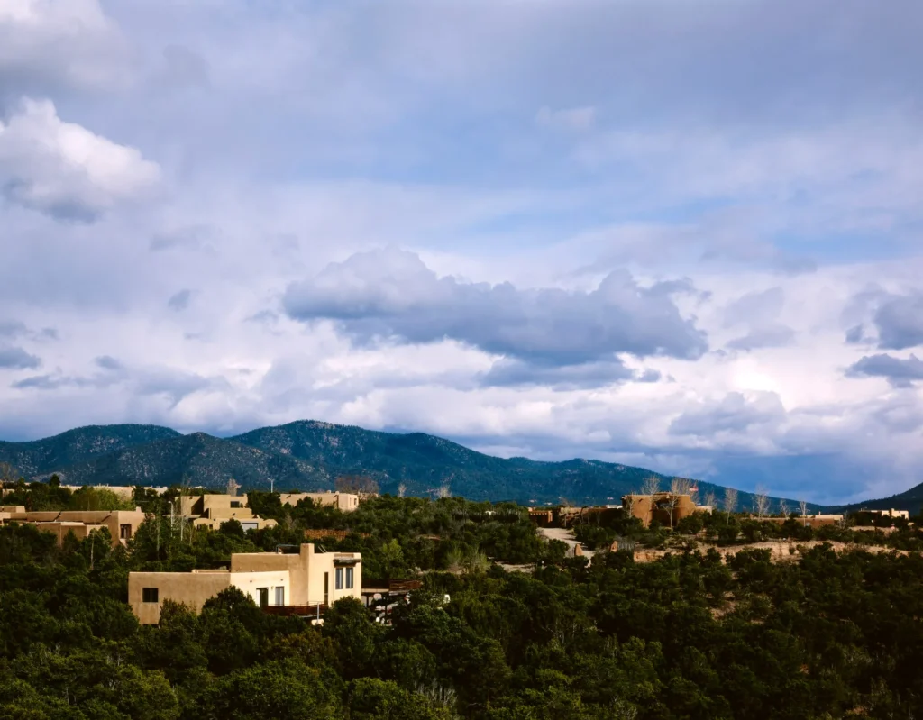 Casas de adobe y montañas con nubes de tormenta en Santa Fe, capital donde se gestiona el registro y la placa temporal en Nuevo México