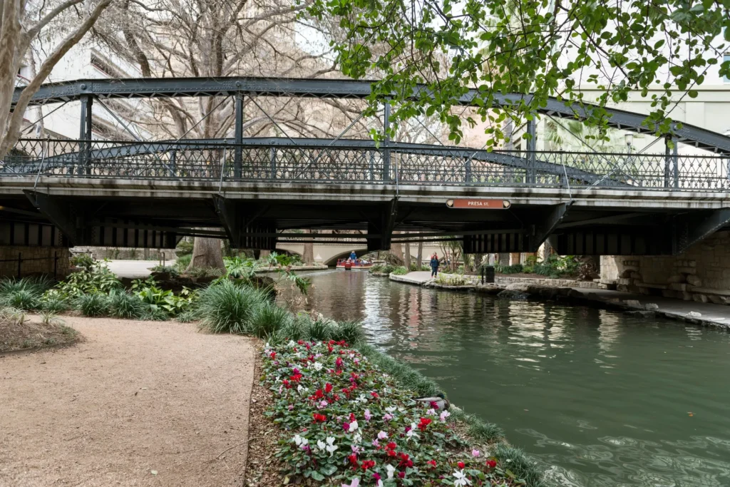 Puente sobre el River Walk de San Antonio entre árboles y flores, ciudad del corredor I-35 donde pedir placa temporal en Texas