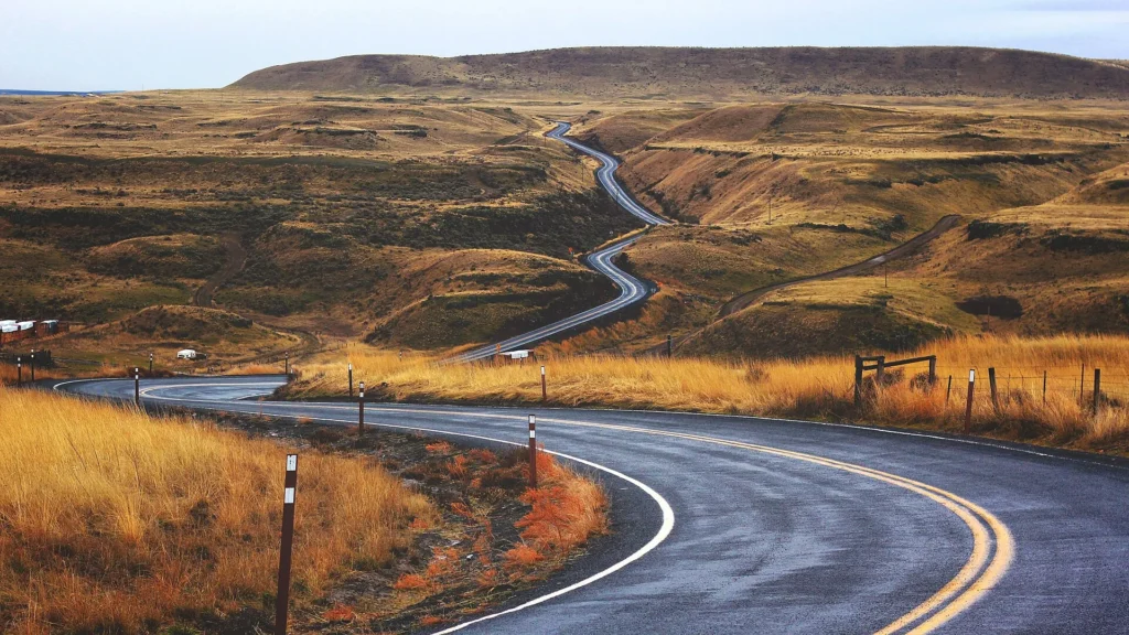 Carretera de dos carriles serpenteando entre colinas secas del este de Washington, ruta típica para manejar con placa temporal en Washington
